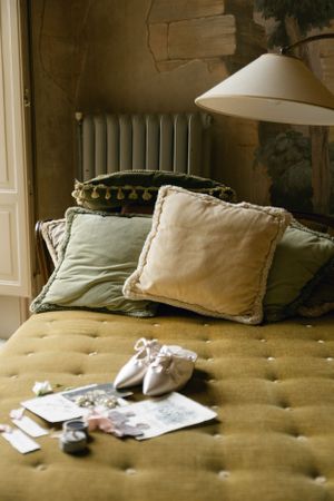 A cozy bedroom corner with olive green cushions, vintage photos, and a white lampshade.
