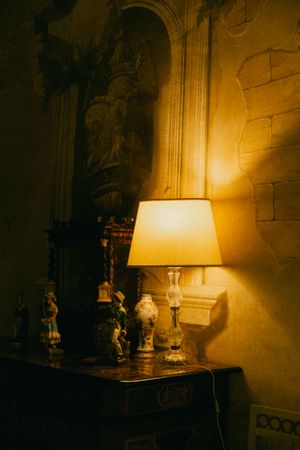 A warm lit interior scene with an antique lamp casting golden light on ornate wall details.