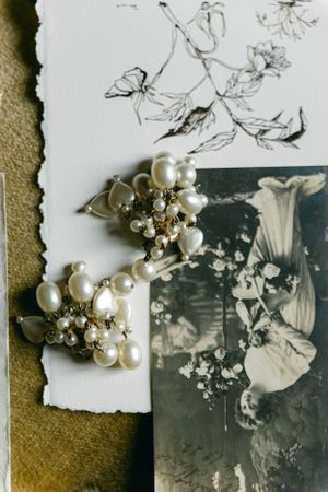 Pearl and crystal brooches rest beside a vintage black and white photograph and delicate floral sketches.