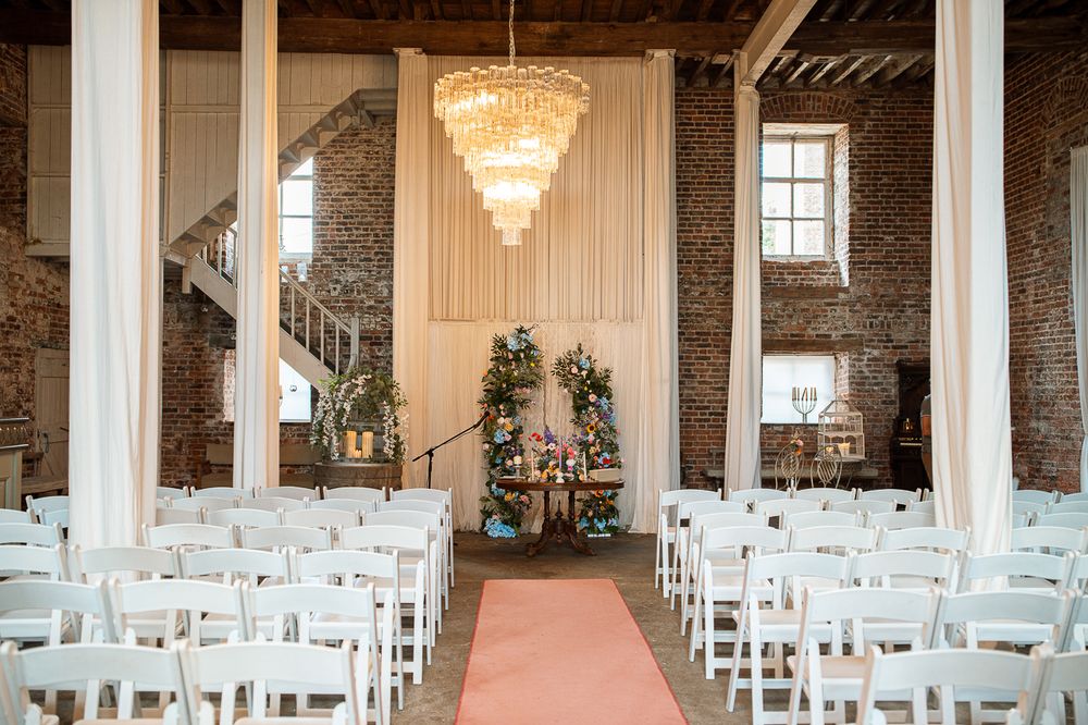 Wedding ceremony venue with white chairs and crystal chandeliers in an industrial brick-walled space.