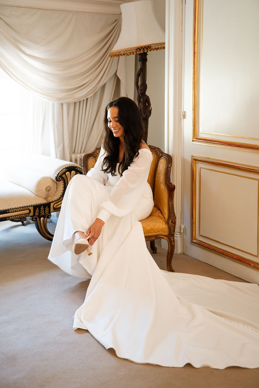 Elegant white wedding dress flowing across a carpeted floor in a room with ornate gold-framed walls.