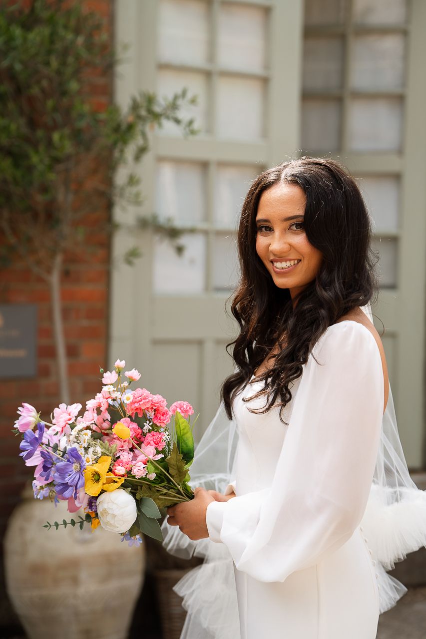 Bridal portrait session with colorful spring flowers against a brick building exterior.