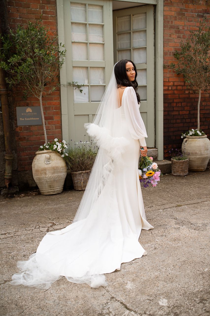 Flowing white wedding gown and veil photographed against rustic brick wall and garden pots.