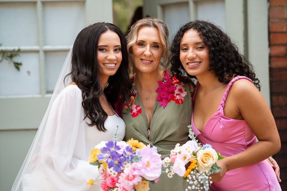 Bridal party in pink dresses holding vibrant bouquets pose together outdoors.