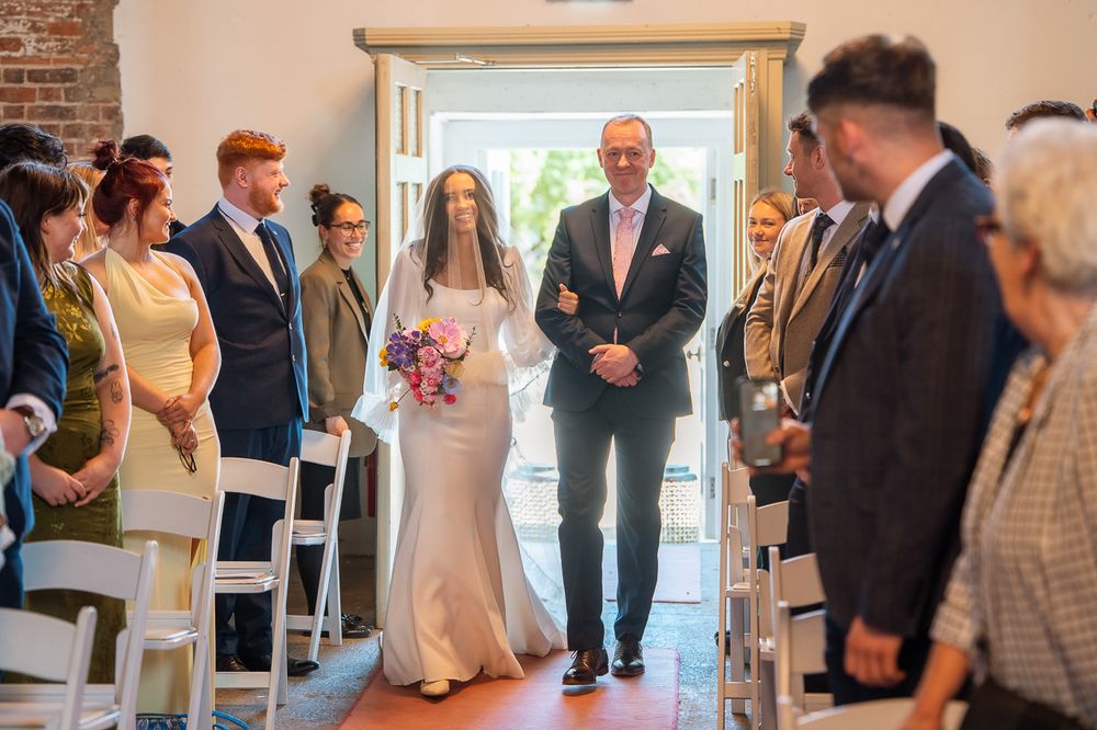 Wedding ceremony guests seated in rows watching proceedings in an elegant indoor venue.