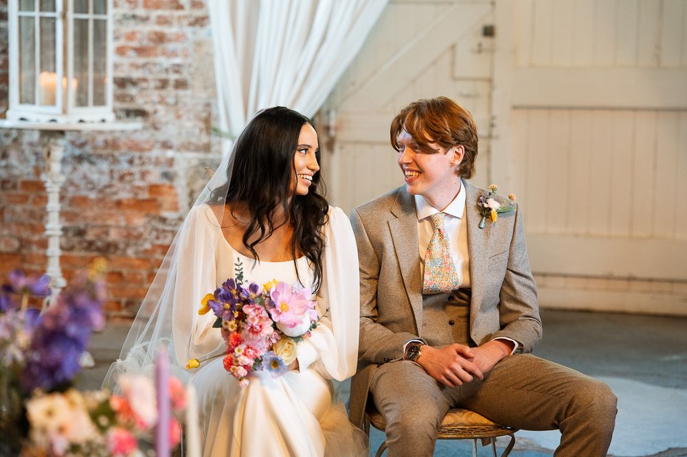 Wedding couple shares intimate moments in a rustic brick-walled venue with white curtains and floral decor.