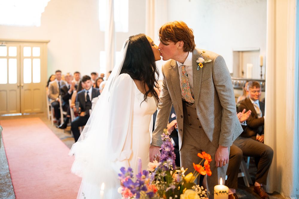Wedding ceremony space with guests seated in rows and purple floral arrangements.