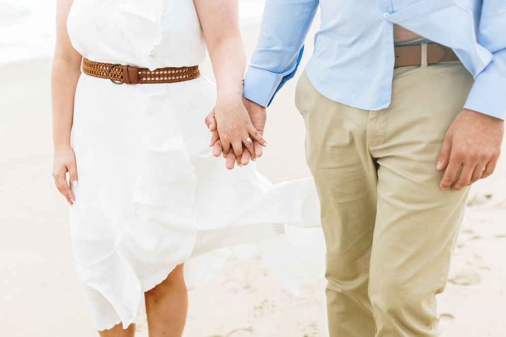 Cropped photo of couple holding hands for engagement photos on cloudy beach day. Seacoast NH Rye Kennebunkport engagement photographer.