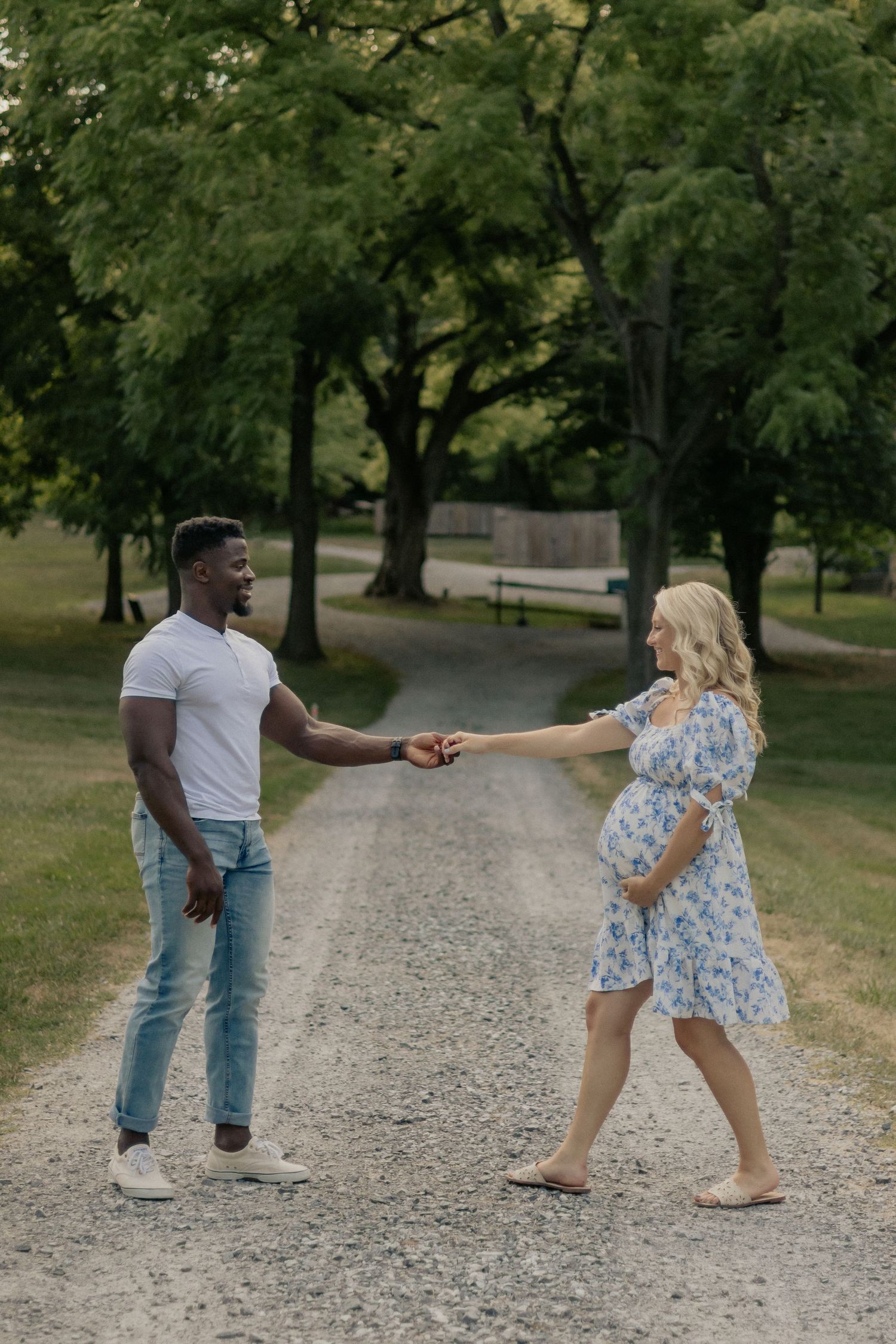 Dancing couple holding hands on gravel path surrounded by trees in park.