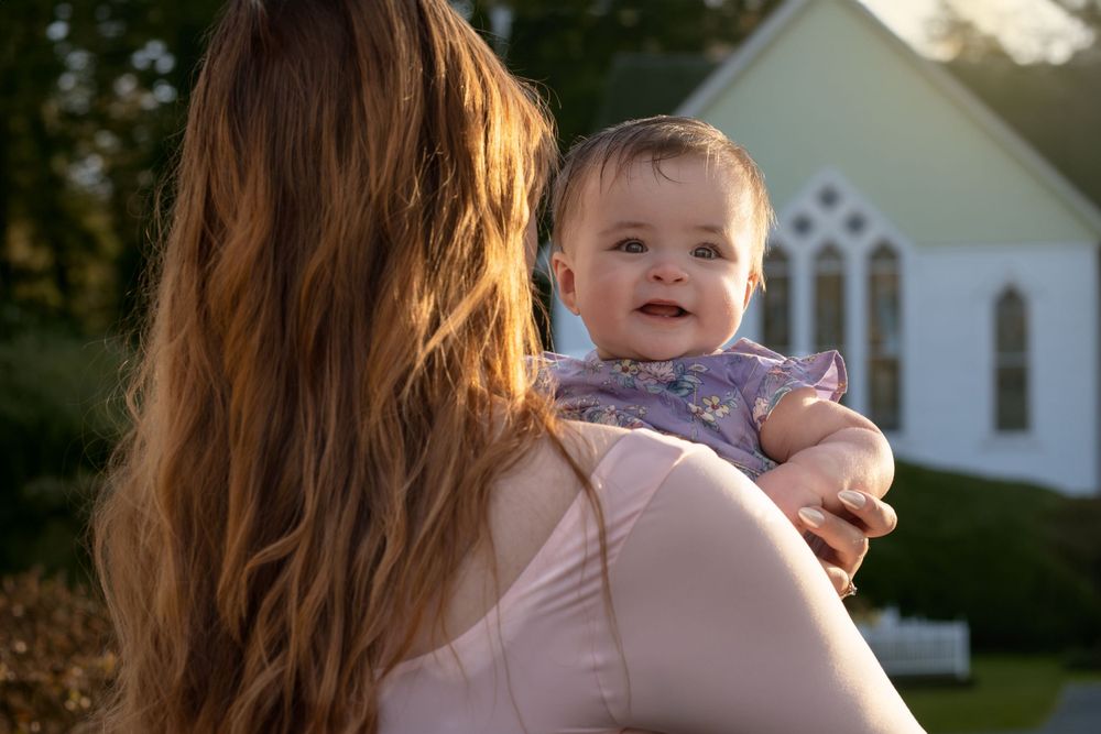 Mother and baby sharing joyful moments in front of a white house at sunset.