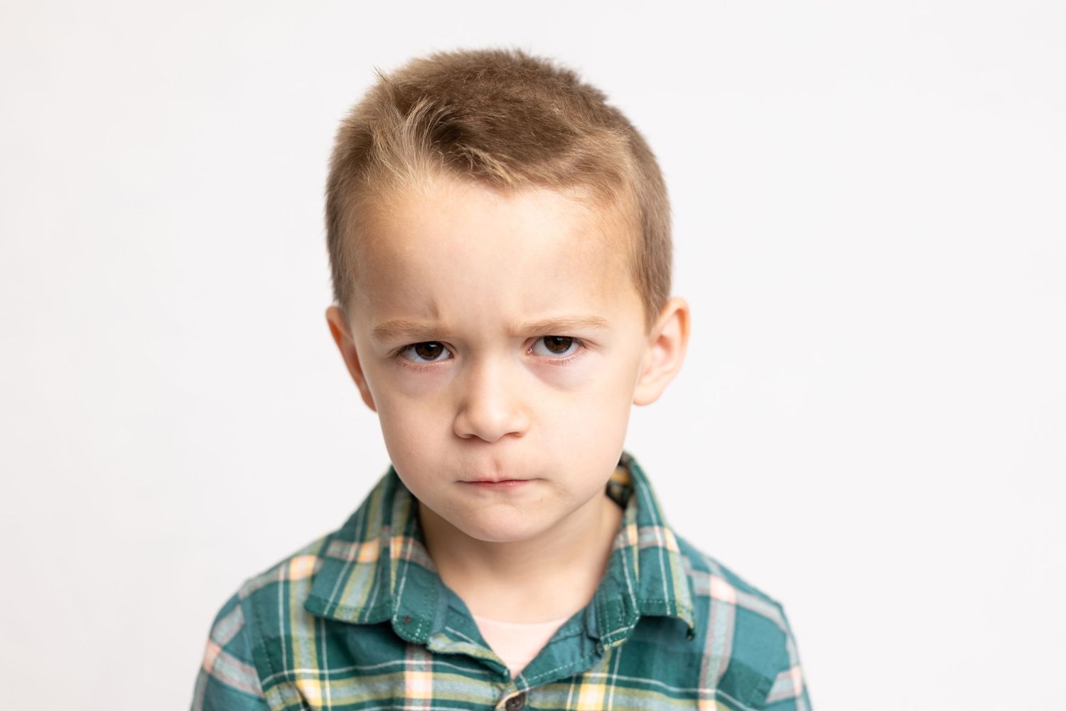 Child in green plaid button-down shirt with neutral expression against white background.