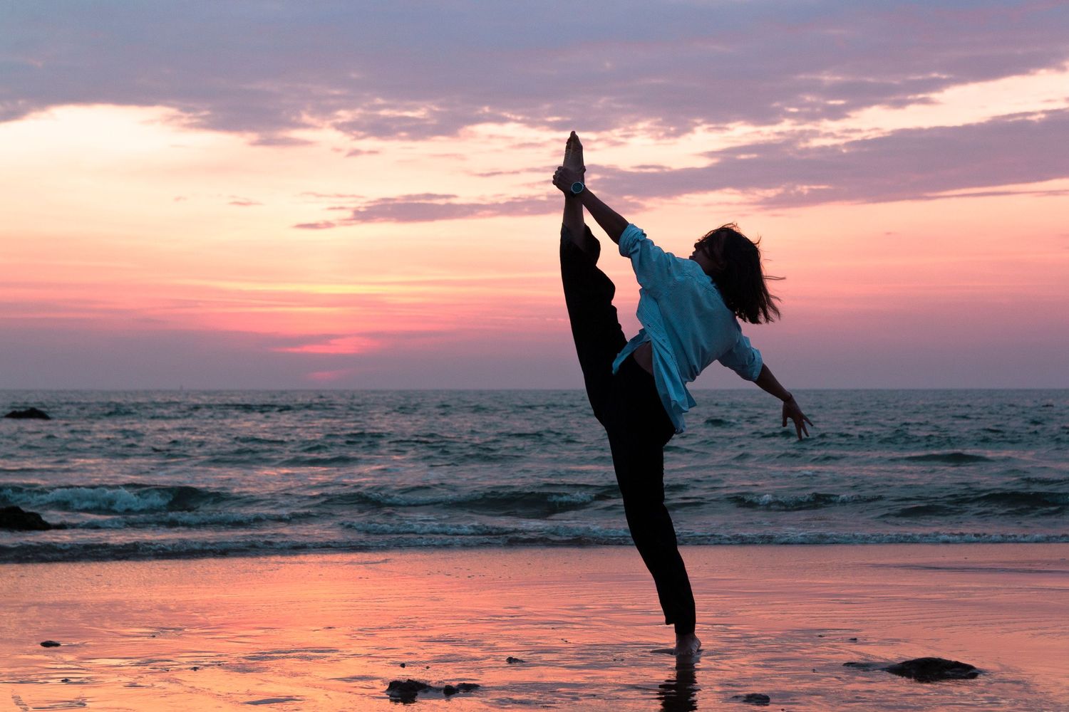 Portrait de danse sur la plage, au coucher de soleil pied dans la main en mouvement.