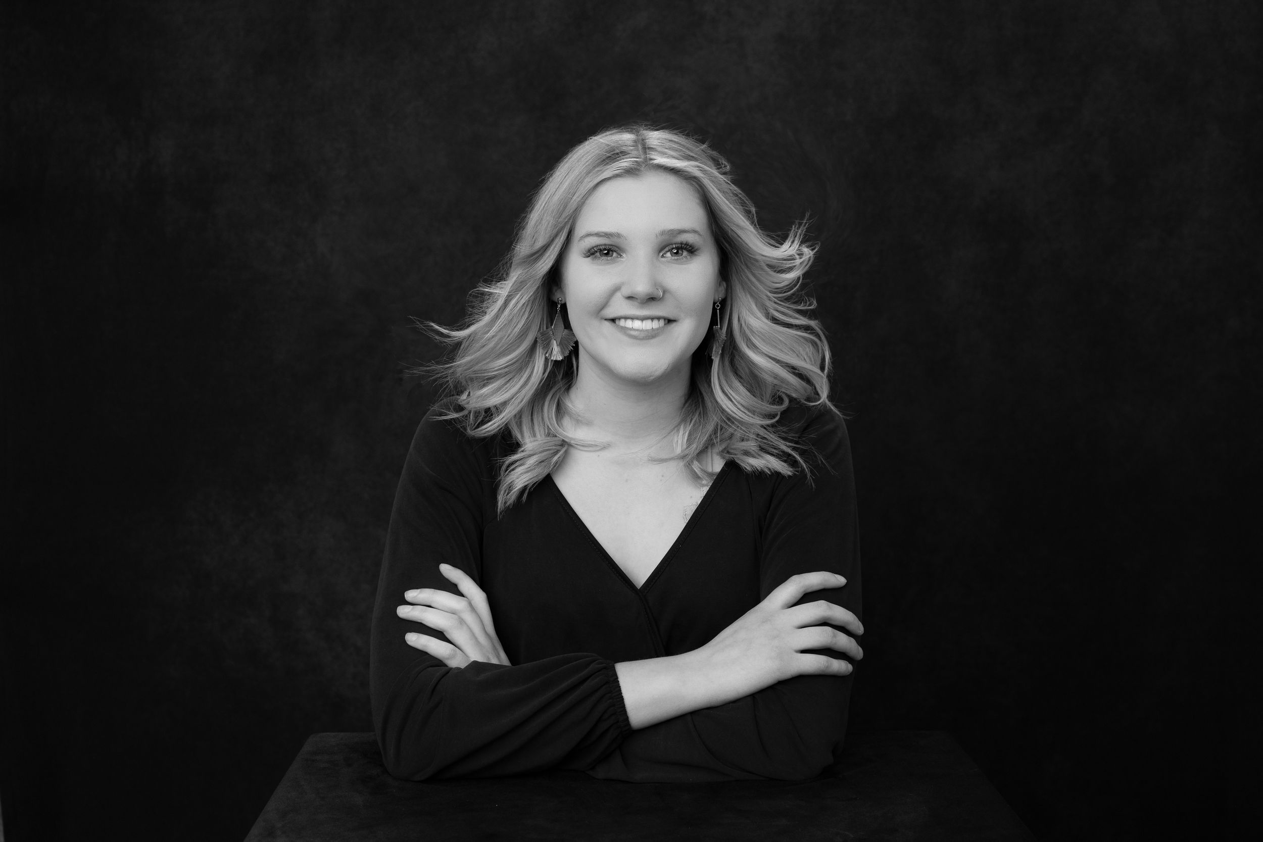 Professional headshot of woman with crossed arms against dark background.