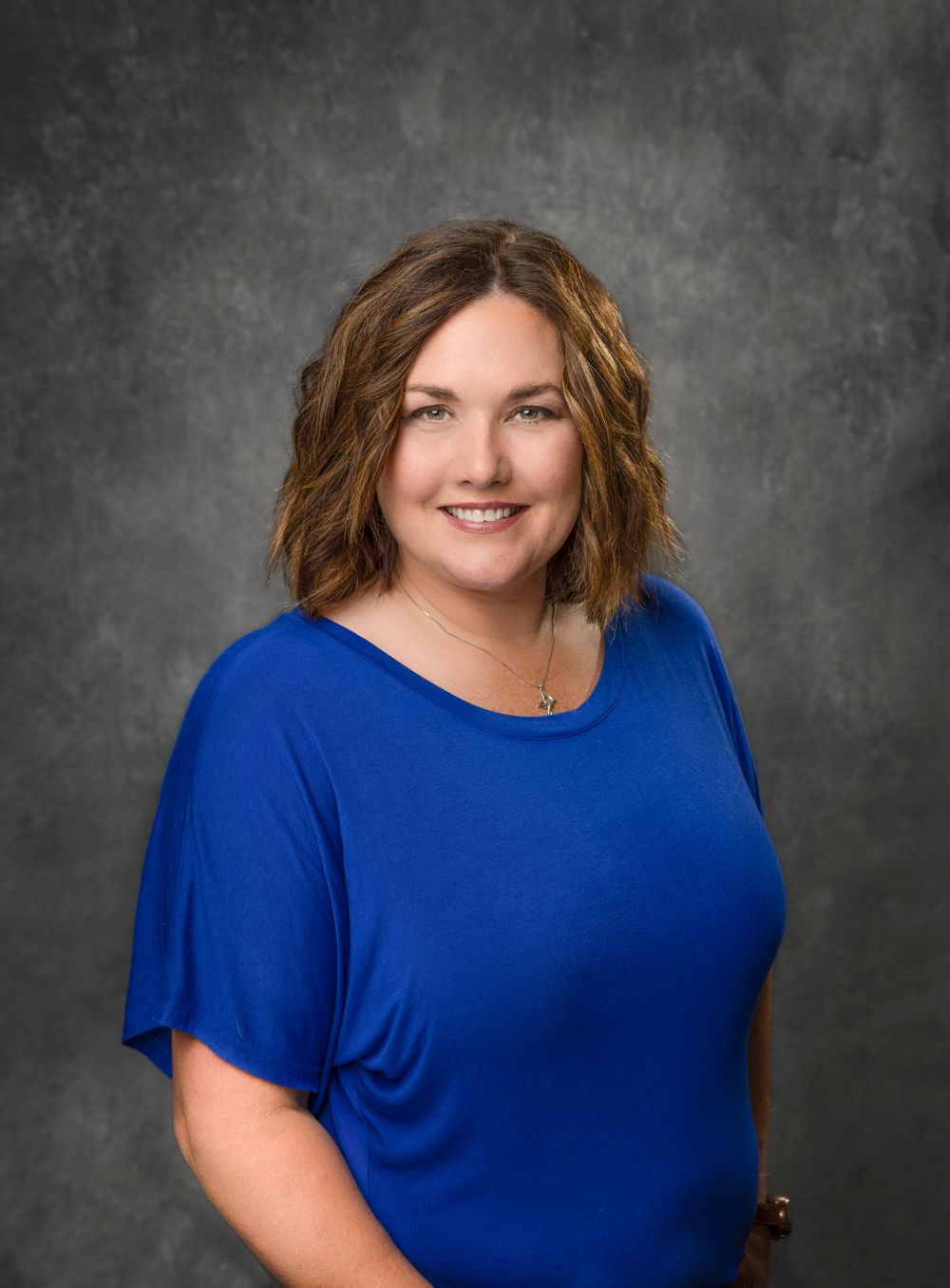 Professional portrait of woman in blue top against textured gray background.