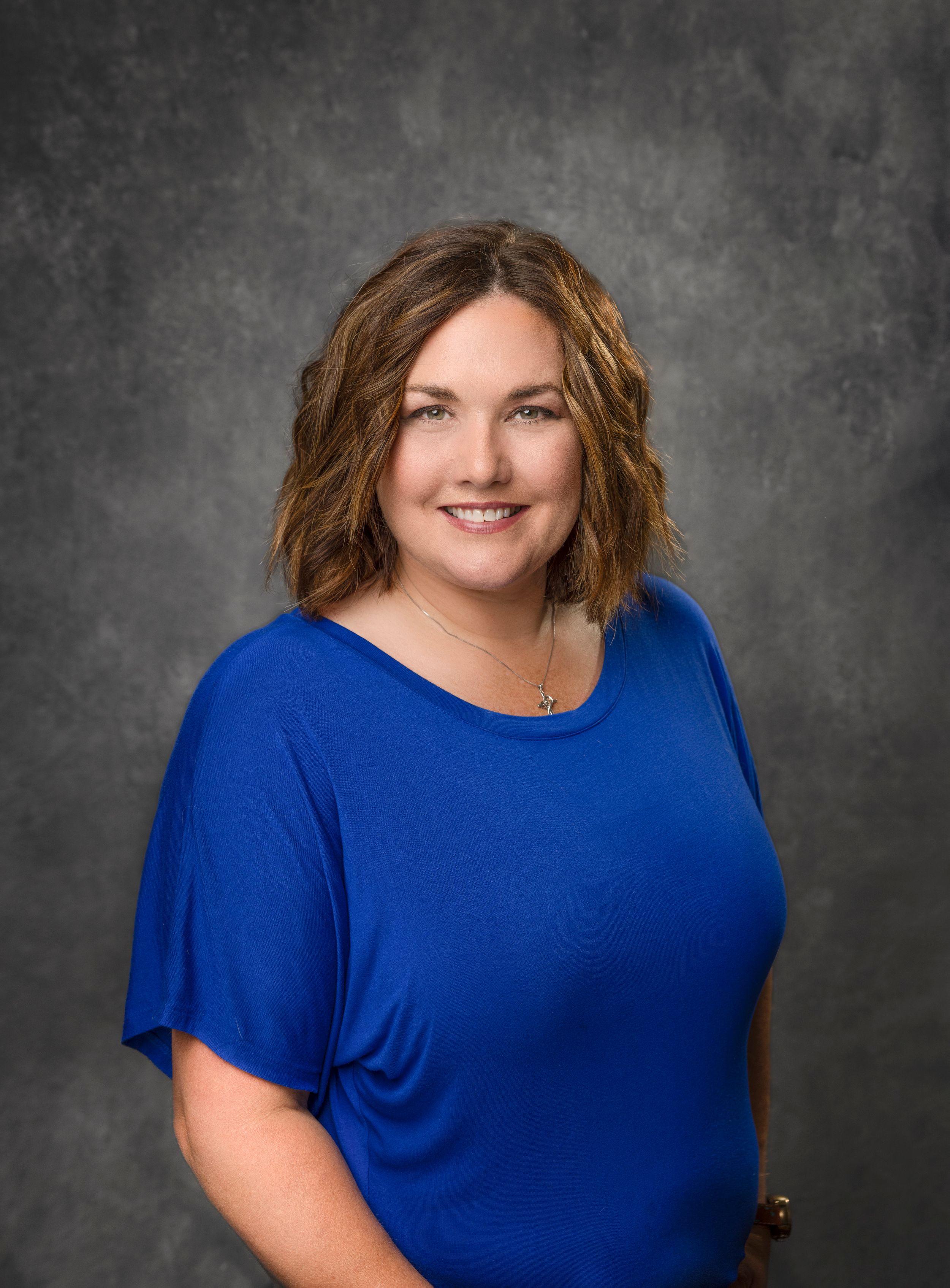 Professional portrait of woman in blue top against textured gray background.