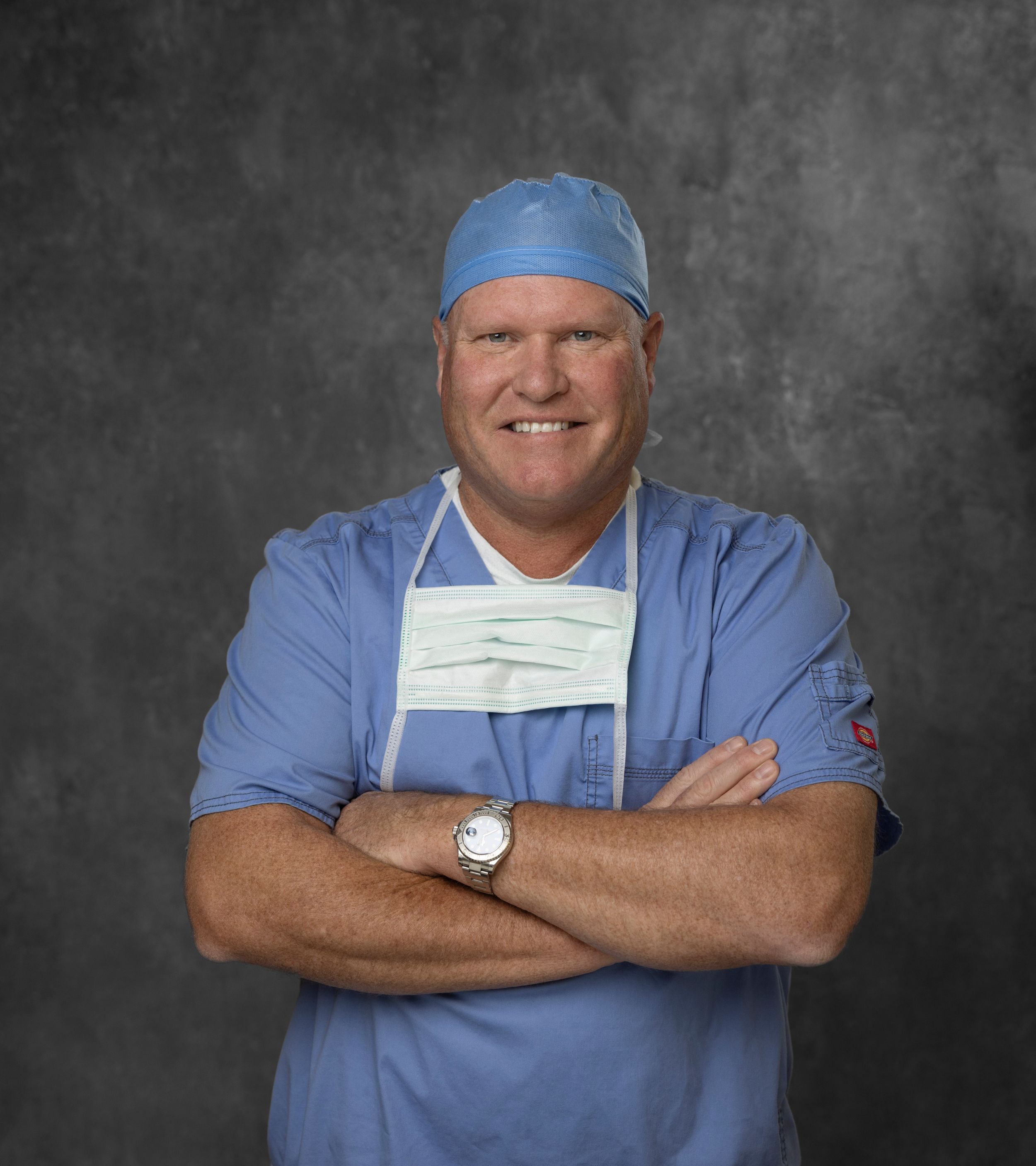 Medical professional in surgical scrubs and cap smiling against gray background.