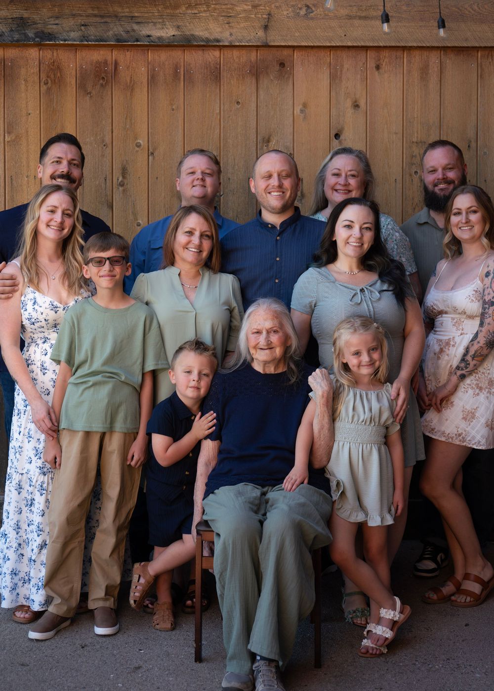 Large multigenerational family portrait posing together indoors against a rustic wooden wall backdrop.