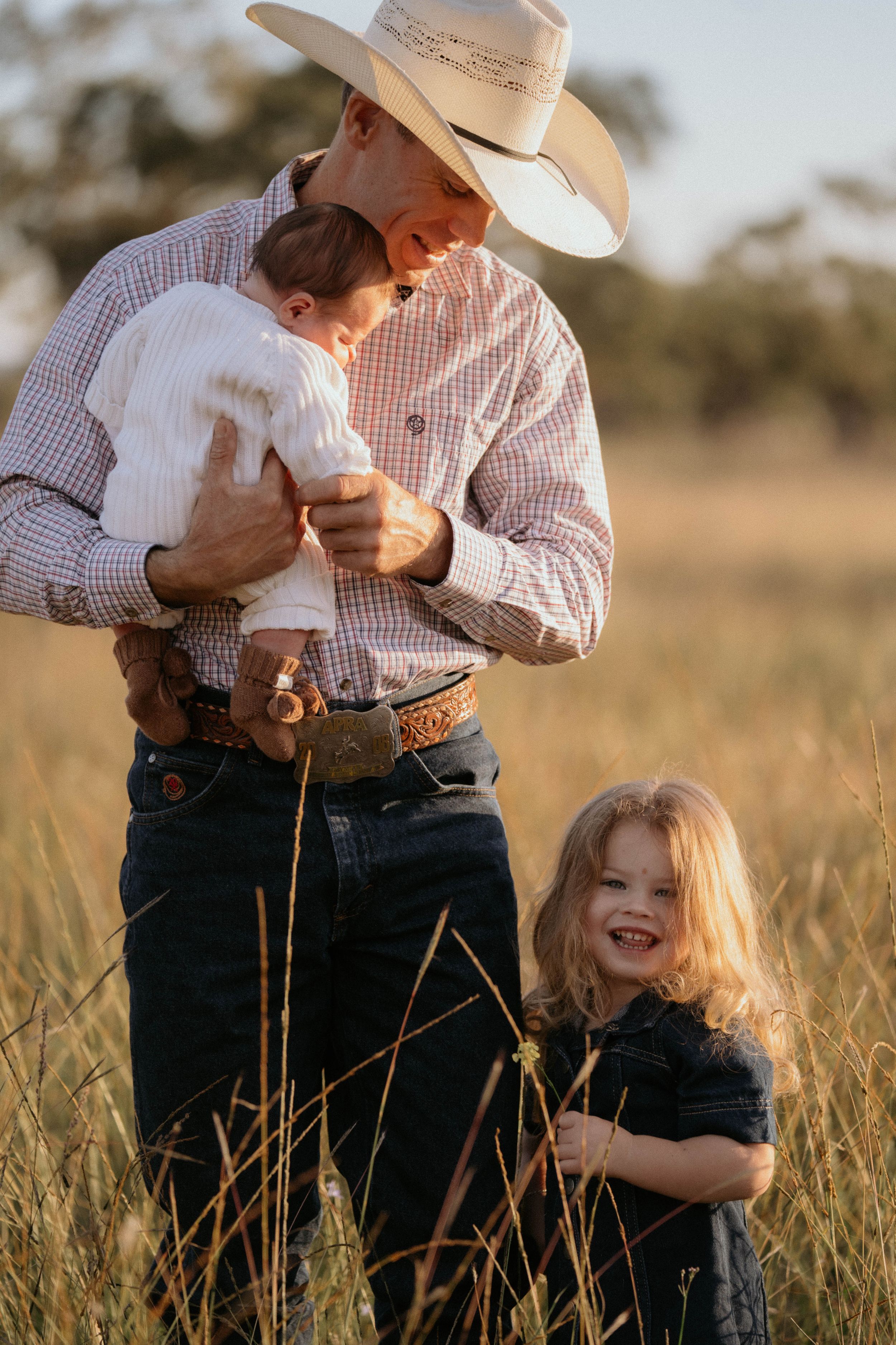 Family in western attire sharing tender moment in golden grass field at sunset.