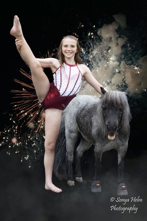 A dance or gymnastics performer poses with an elegant split pose against a backdrop of sparkling fireworks and misty effects.
