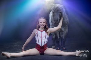 A gymnast performs splits and poses near a horse in a misty blue-lit setting.