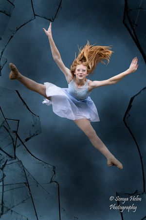 A dancer in white performing graceful leaps and poses against a moody blue background.
