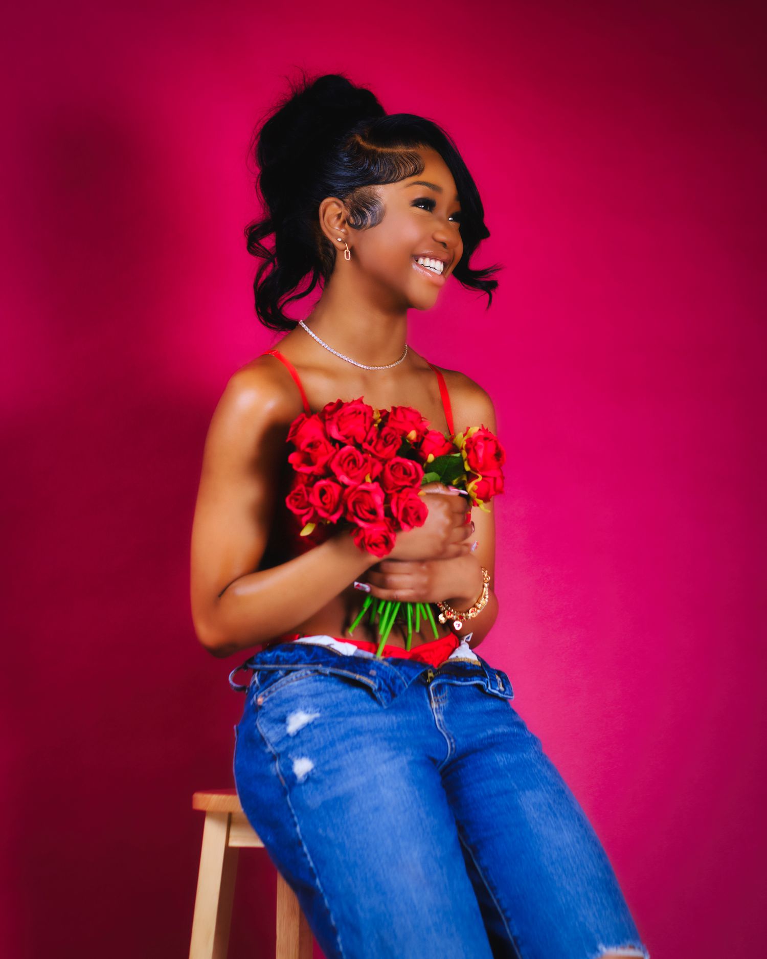 Portrait of someone holding red roses against vibrant pink background wearing jeans.