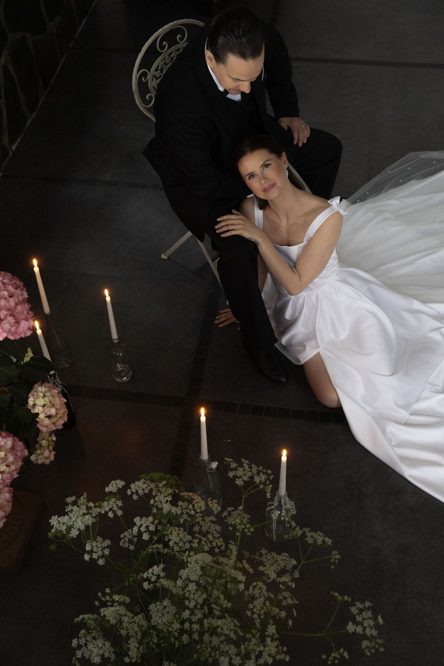 A romantic wedding scene with a bride in white gown and groom surrounded by lit candles and pink floral arrangements.