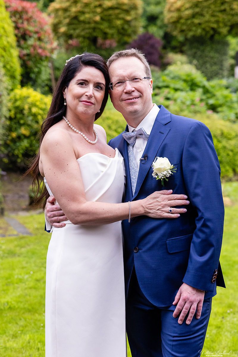 A couple in wedding attire poses against a colorful garden backdrop.