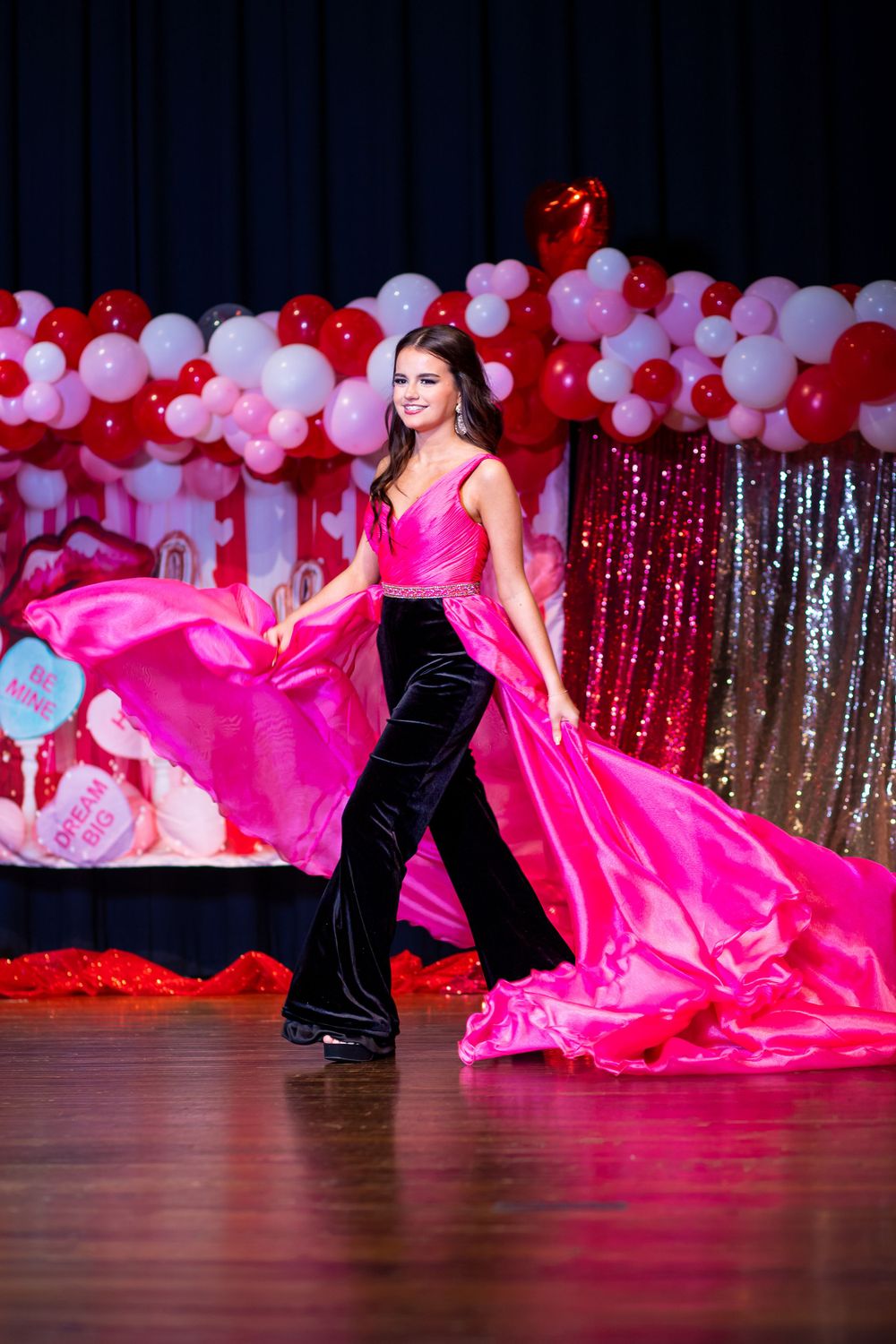 Model showcases pink satin and black velvet ensemble with flowing train on stage.