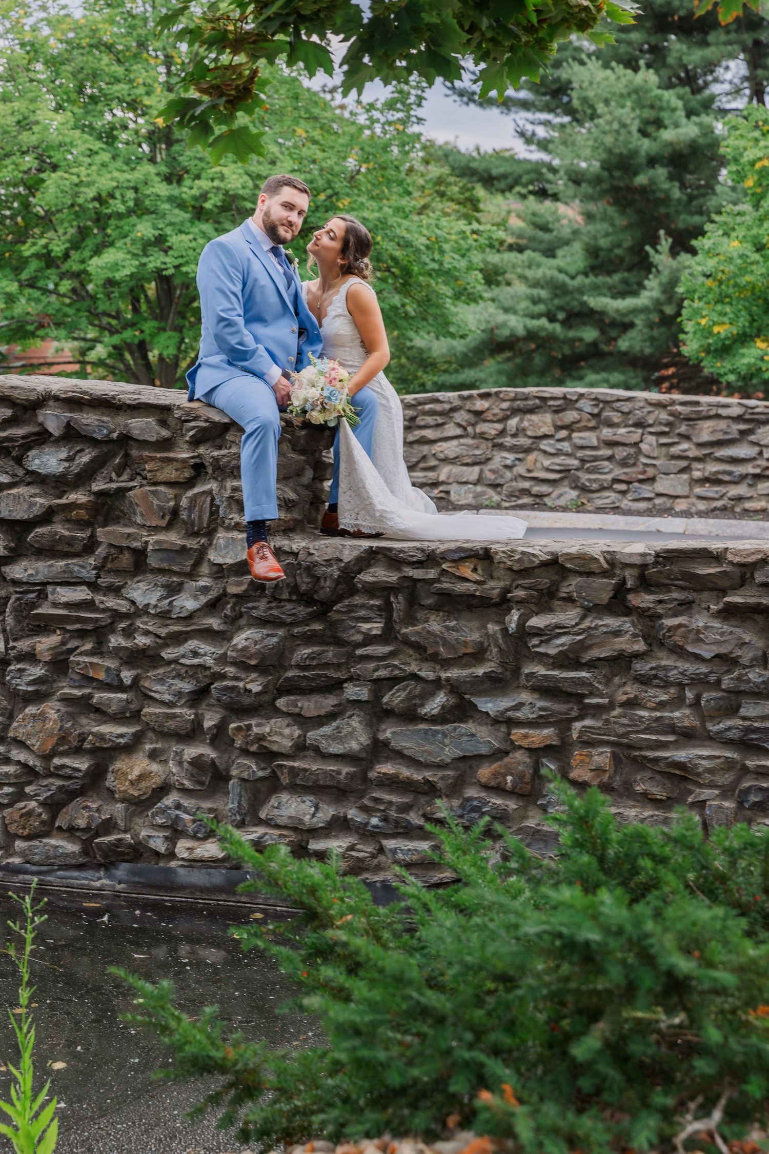 A couple sitting together on a rustic stone wall surrounded by greenery.
