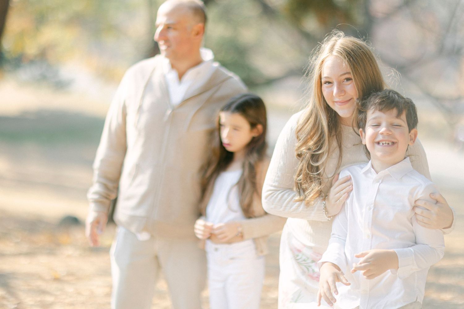 Family group walks together in coordinated white and beige outfits during outdoor photo session.