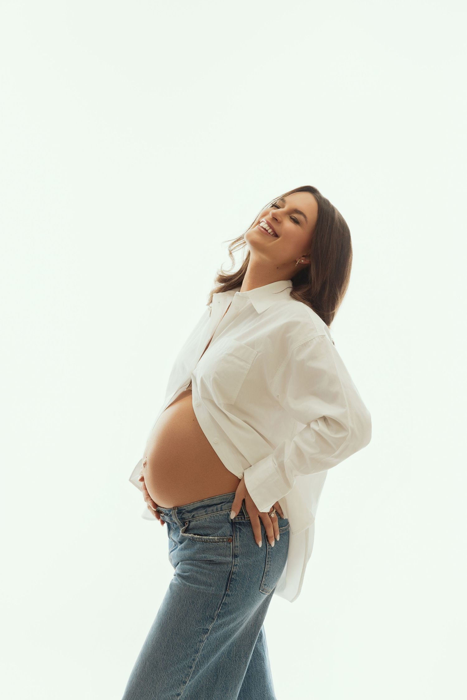 Radiant expectant mother embracing her baby bump in a serene maternity photoshoot in jeans and white shirt