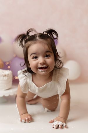 Baby girl celebrating her first birthday with a cake smash and colorful garland backdrop