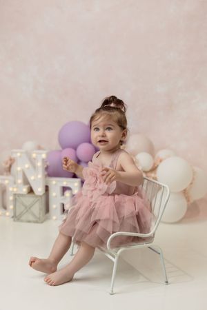 Baby smiling while sitting next to a decorated birthday cake and balloon garland