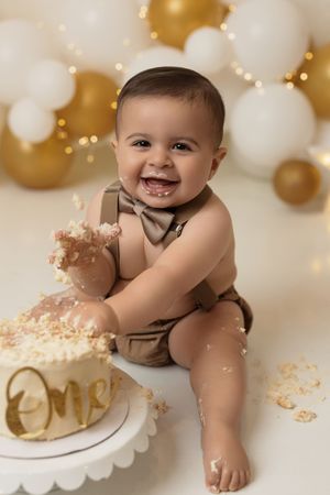 Baby boy enjoying a colorful cake smash with a festive balloon garland backdrop
