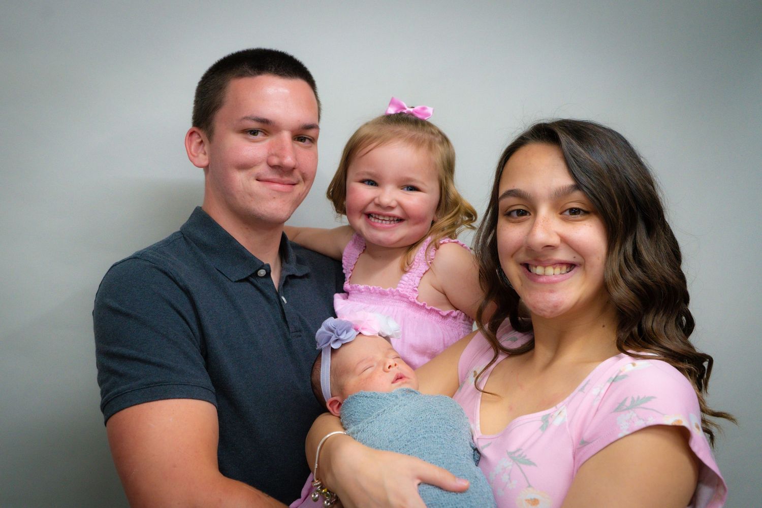 Portrait of multi-ethnic family with three children against black backdrop.