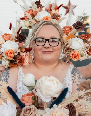 Close up portrait surrounded by a stunning floral arrangement with peach, white and brown roses and dried elements.