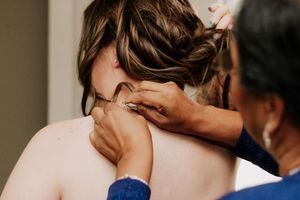 A hairstylist works on styling a bride's updo during wedding preparations.