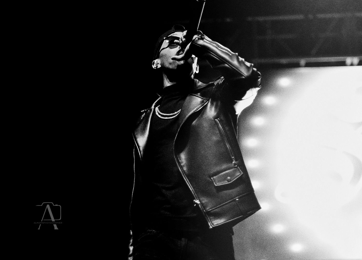 Silhouetted performer in leather jacket on stage in dramatic black and white lighting.