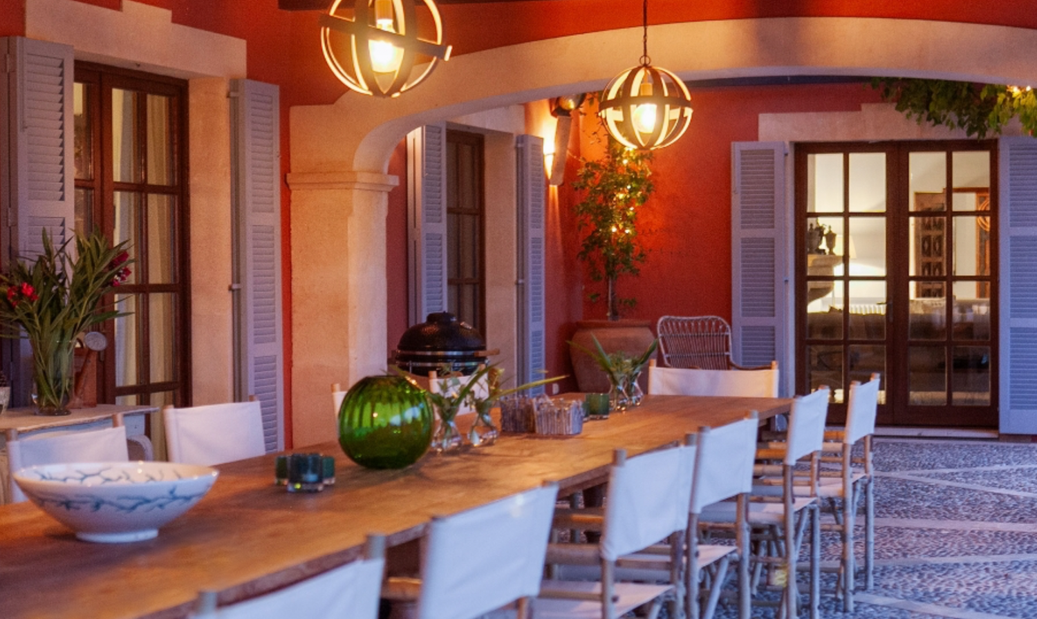 Rustic dining room with wooden table, white chairs, and warm lighting from globe pendant lamps.