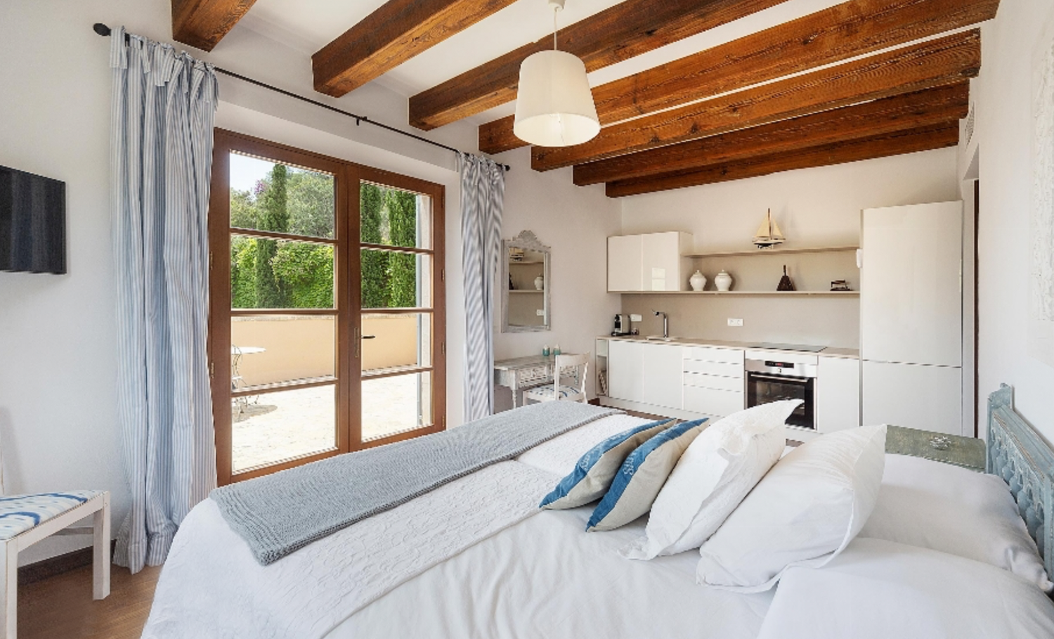 Modern bedroom with exposed beams, white bedding, and sliding glass doors leading to outdoor patio.