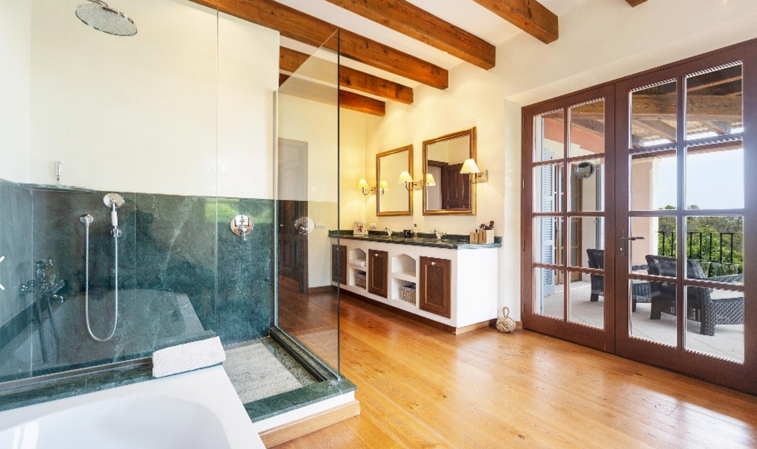 Modern bathroom with glass shower enclosure, wooden beams, and French doors opening to terrace.