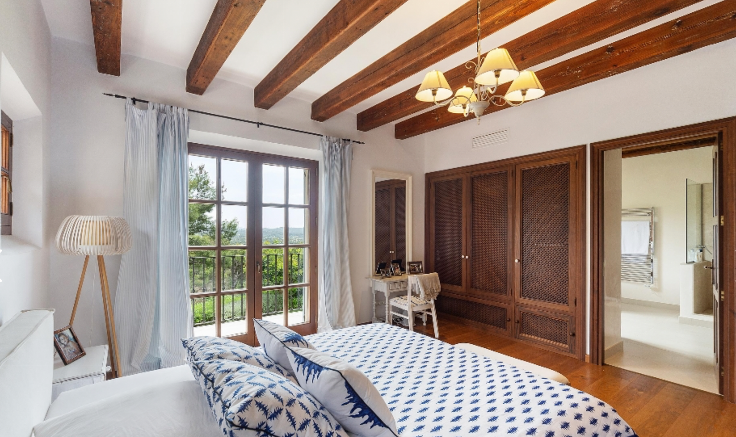Elegant bedroom featuring exposed wooden beams, built-in wardrobes, and windows with garden views.