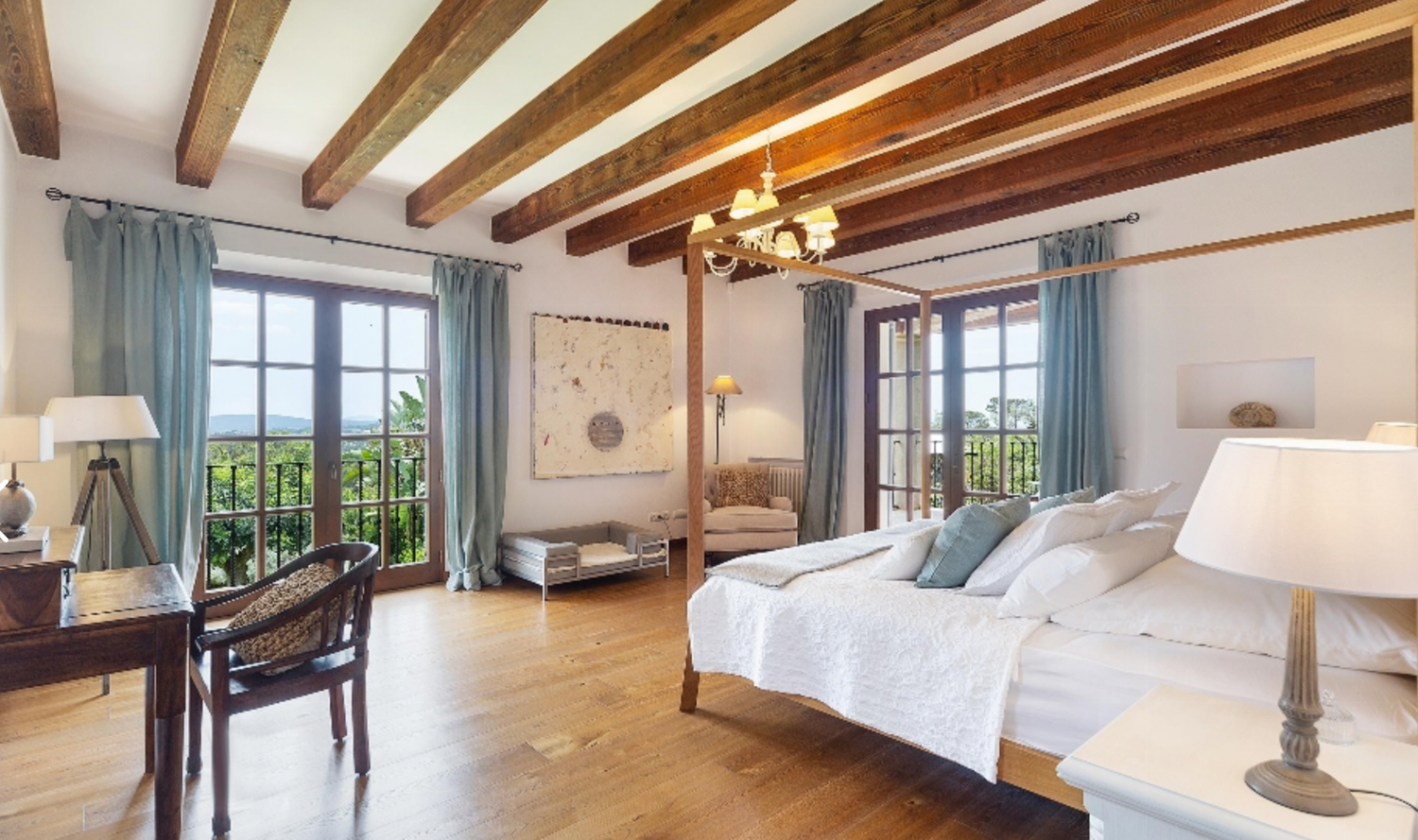 Luxurious Mediterranean bedroom with exposed wooden beams, white bedding, and French doors opening to a scenic balcony.