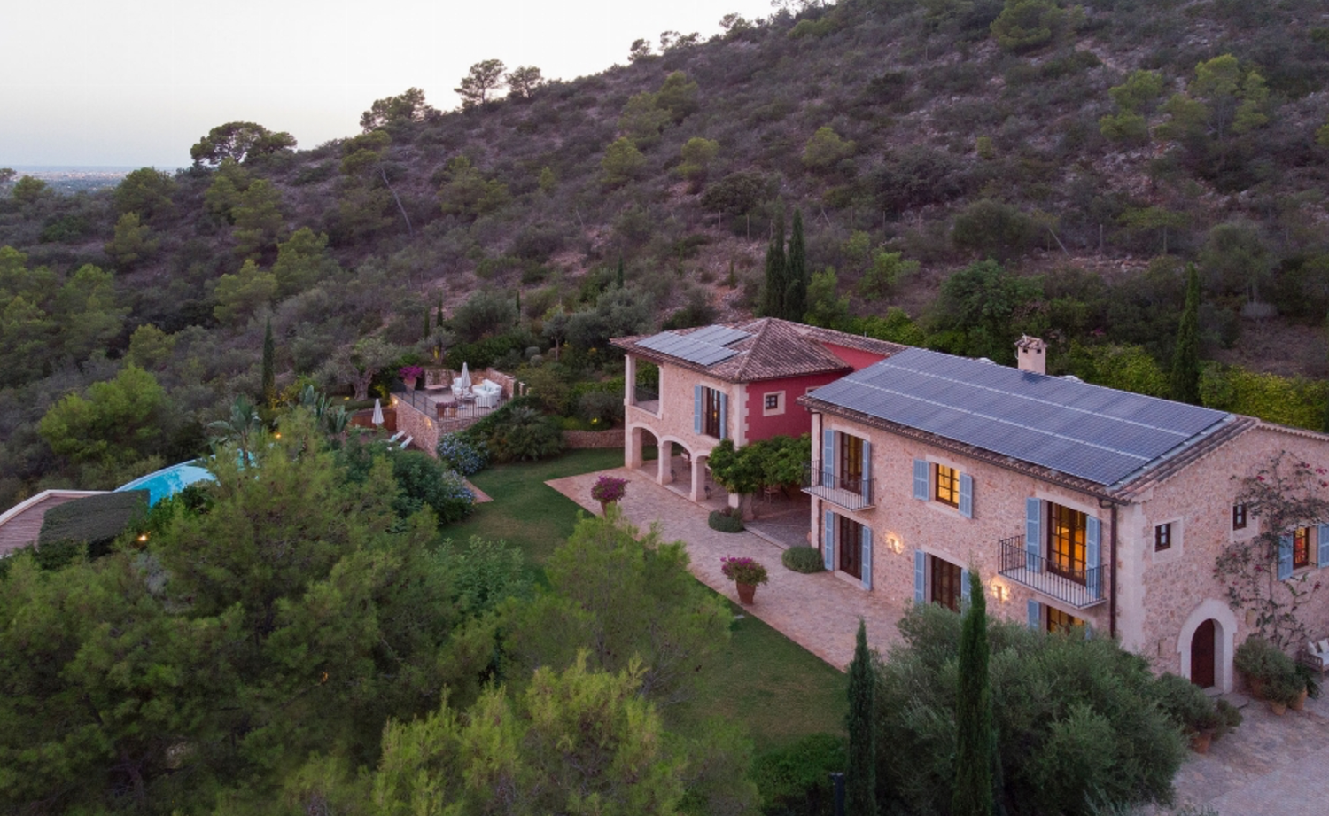 Aerial view of a pink and peach Mediterranean villa nestled in a hillside with solar panels on the roof.