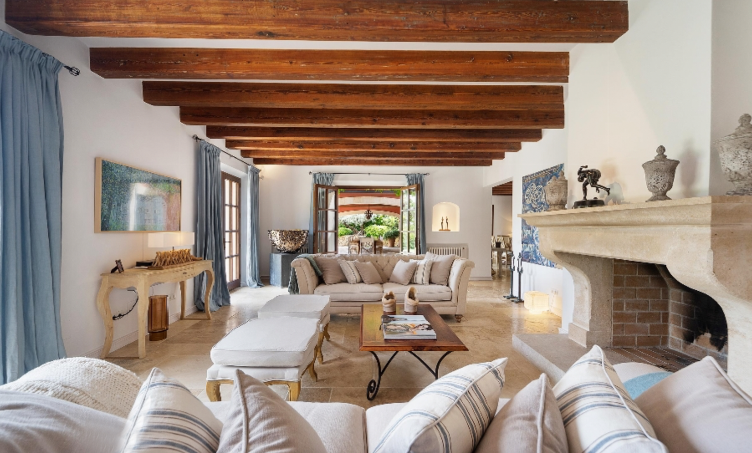 Elegant living room with exposed wooden beams, comfortable white sofas, and a large stone fireplace.
