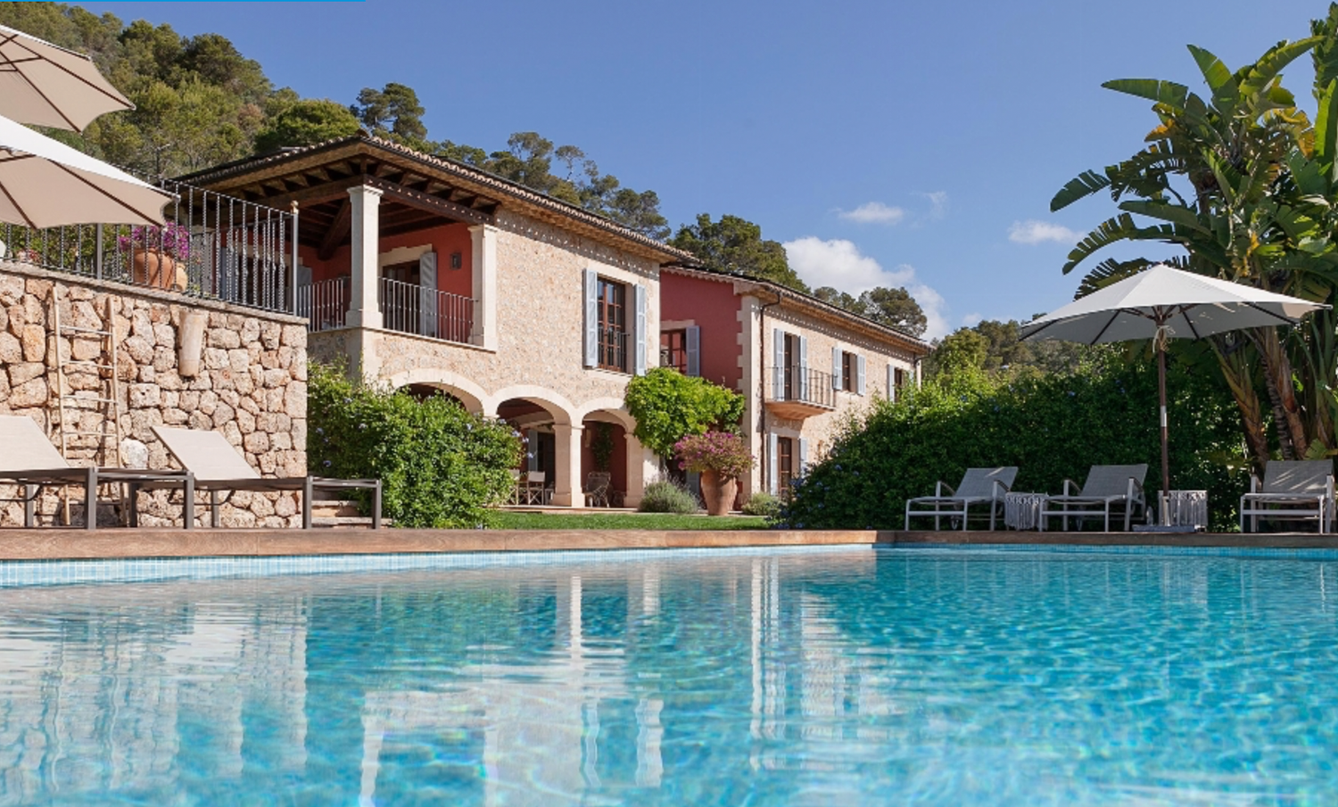 Mediterranean villa with stone facade and swimming pool surrounded by lush landscaping.