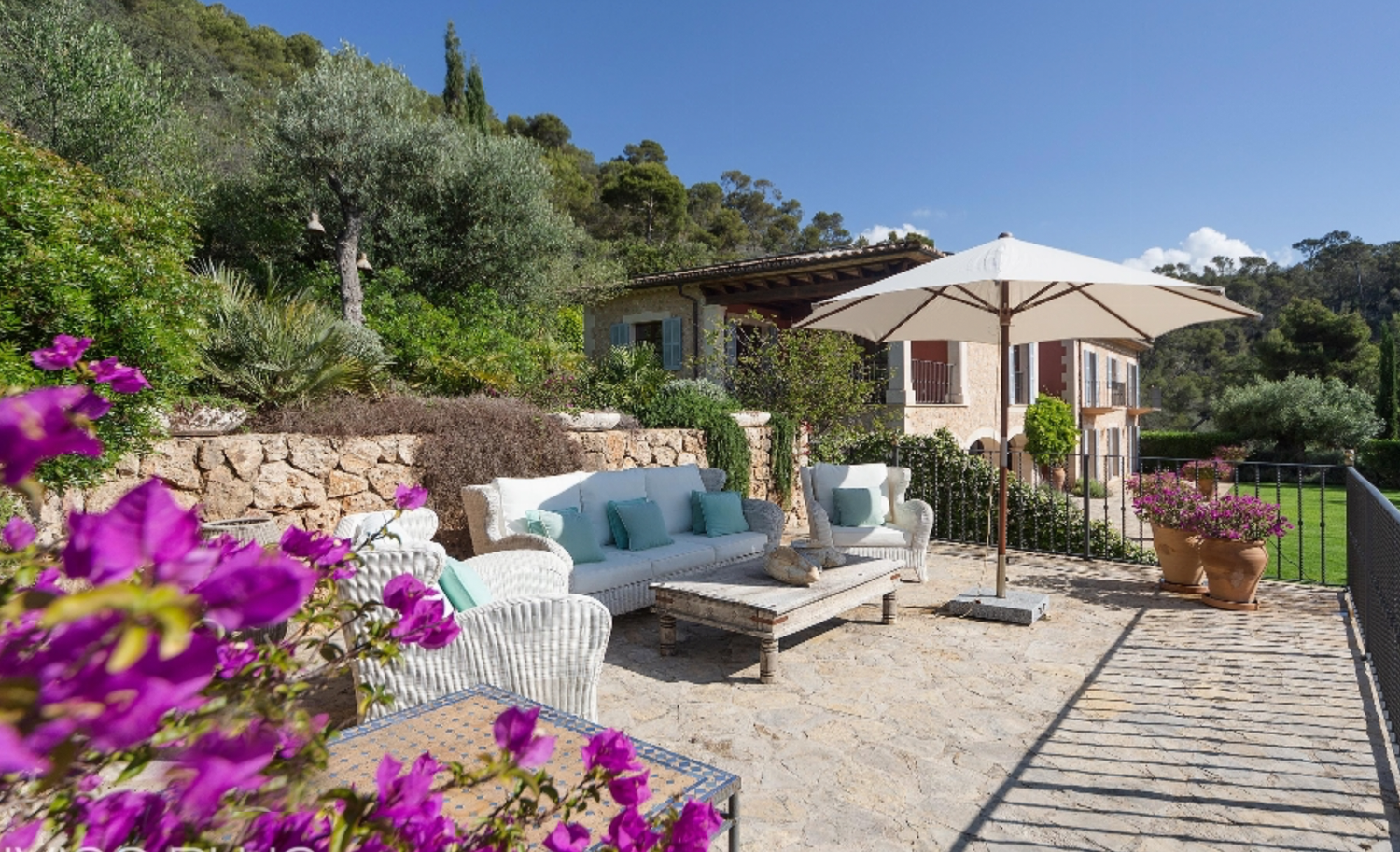 Outdoor patio with chaise lounges, pink flowers, and mountain views at a Mediterranean villa.