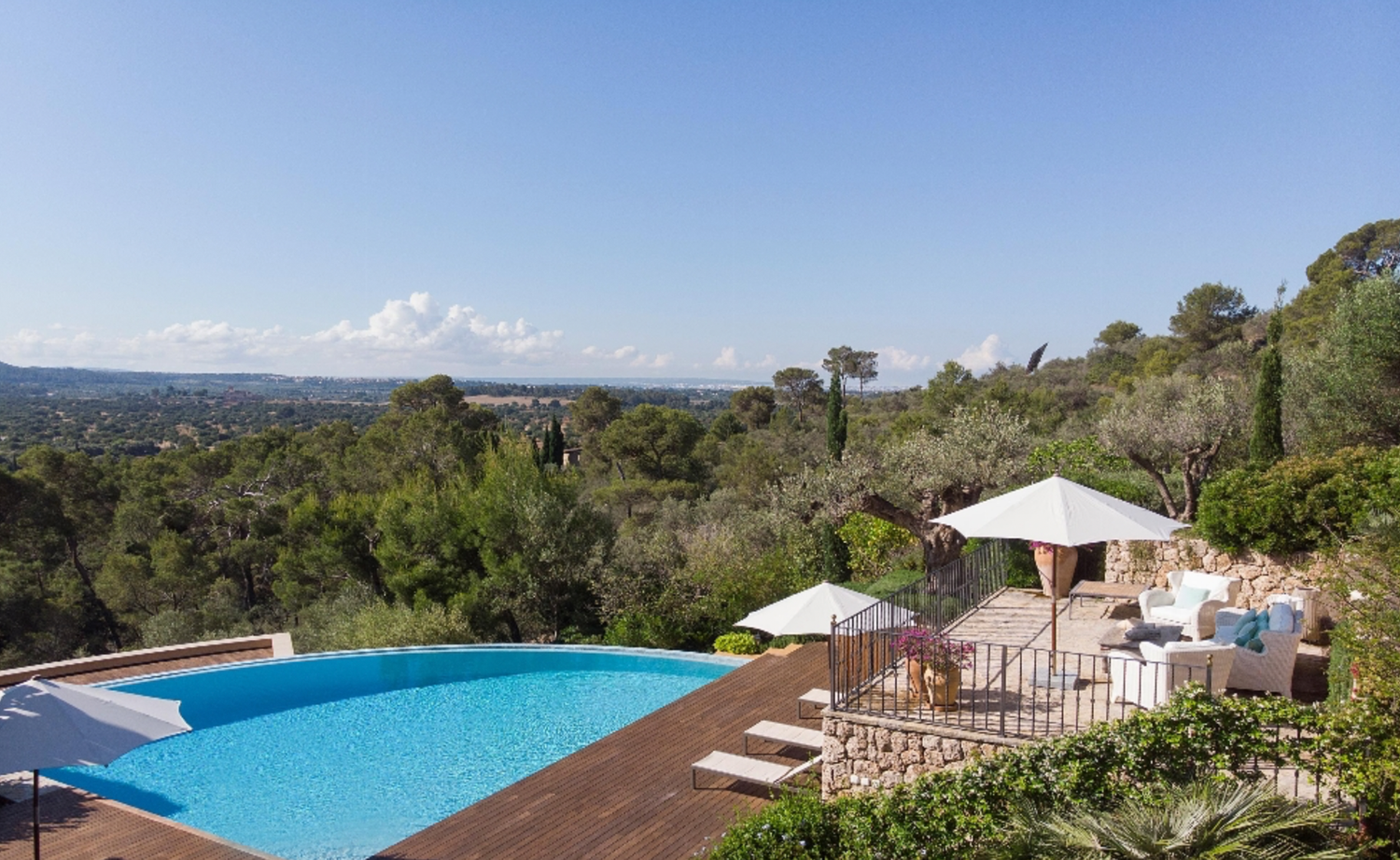 Panoramic hilltop infinity pool overlooking a vast landscape with umbrella seating.