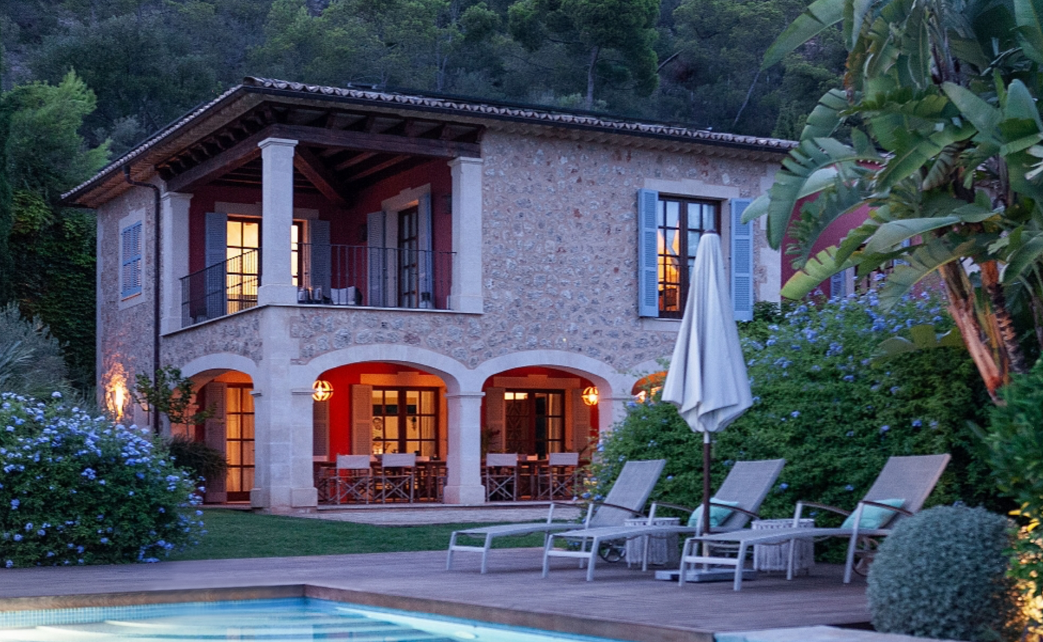 Mediterranean-style villa with arched windows and pool deck at dusk.